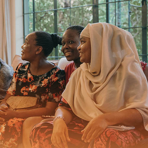 Three Kenyan women smiling, sitting on a couch