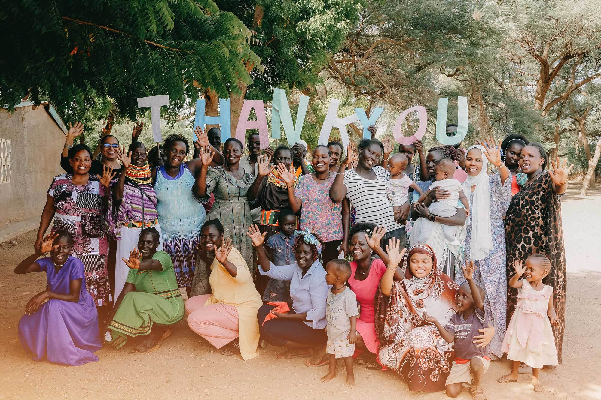 large group of Kenyan women and children smiling and holding up the letter that say THANK YOU